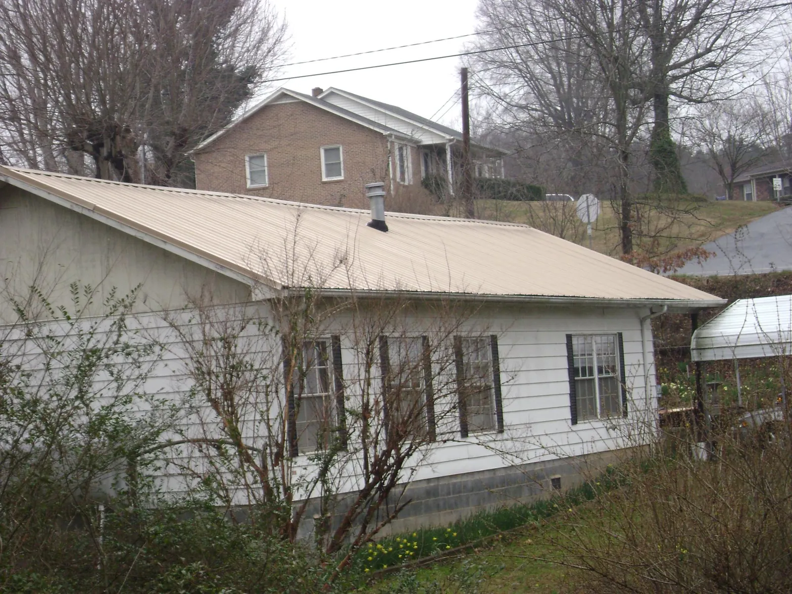 Tan metal roof on a white sided house set into a hillside — Commercial Roofing by Roofing Brothers in Larkspur